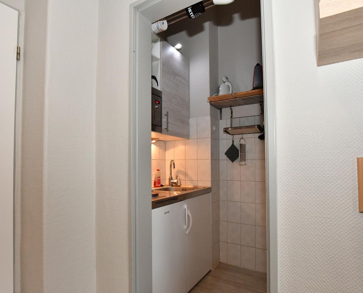 Küche mit Spüle, Kühlschrank und Mikrowelle. Wandverkleidung und Holzboden.