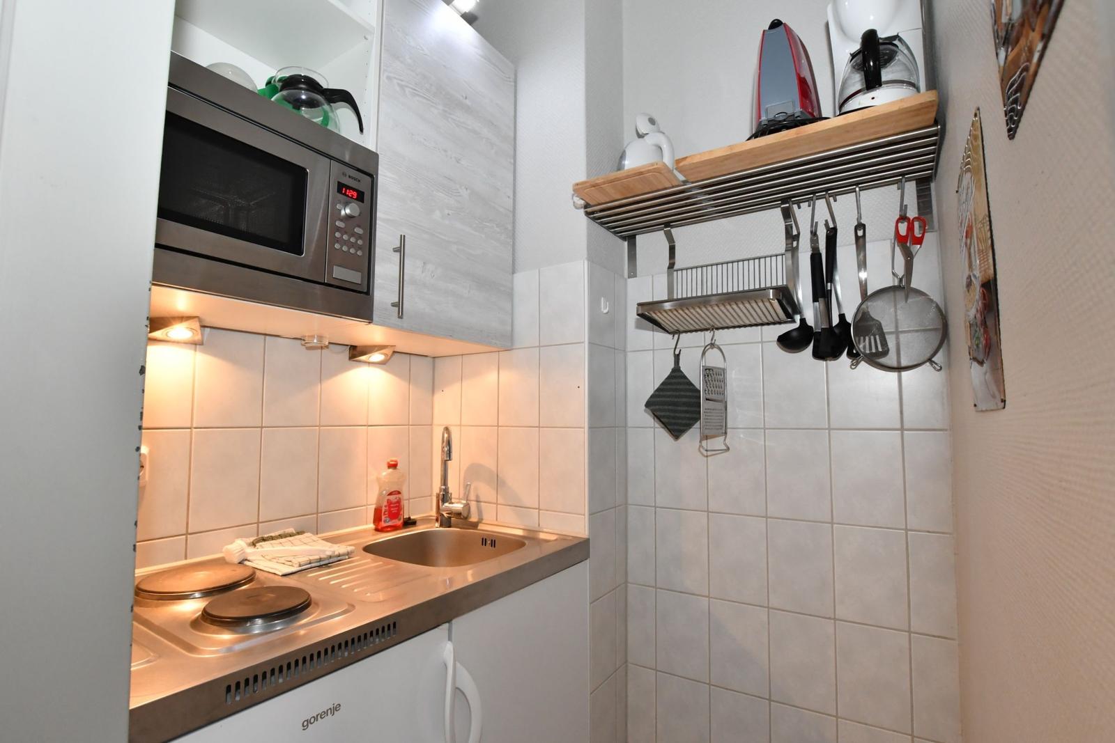 Küche mit Herd, Spüle, Mikrowelle und Hängeschrank mit Küchenutensilien.