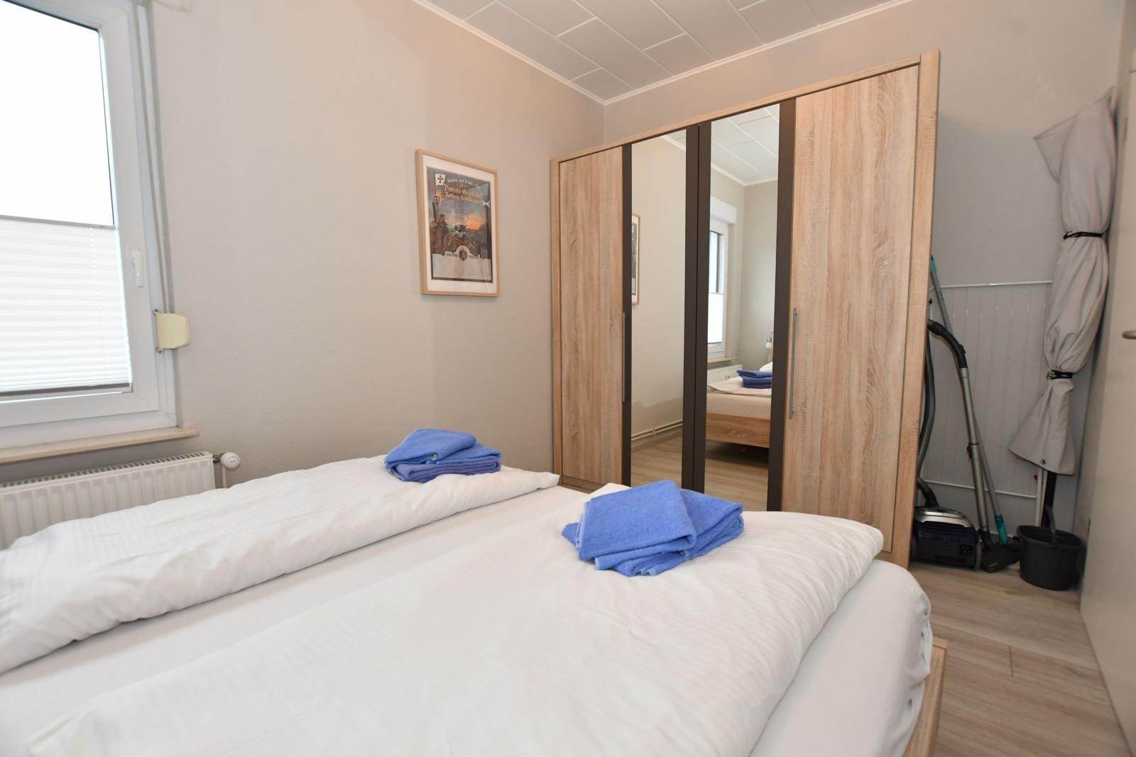 Schlafzimmer mit Doppelbett, Spiegelschrank und Fenster.