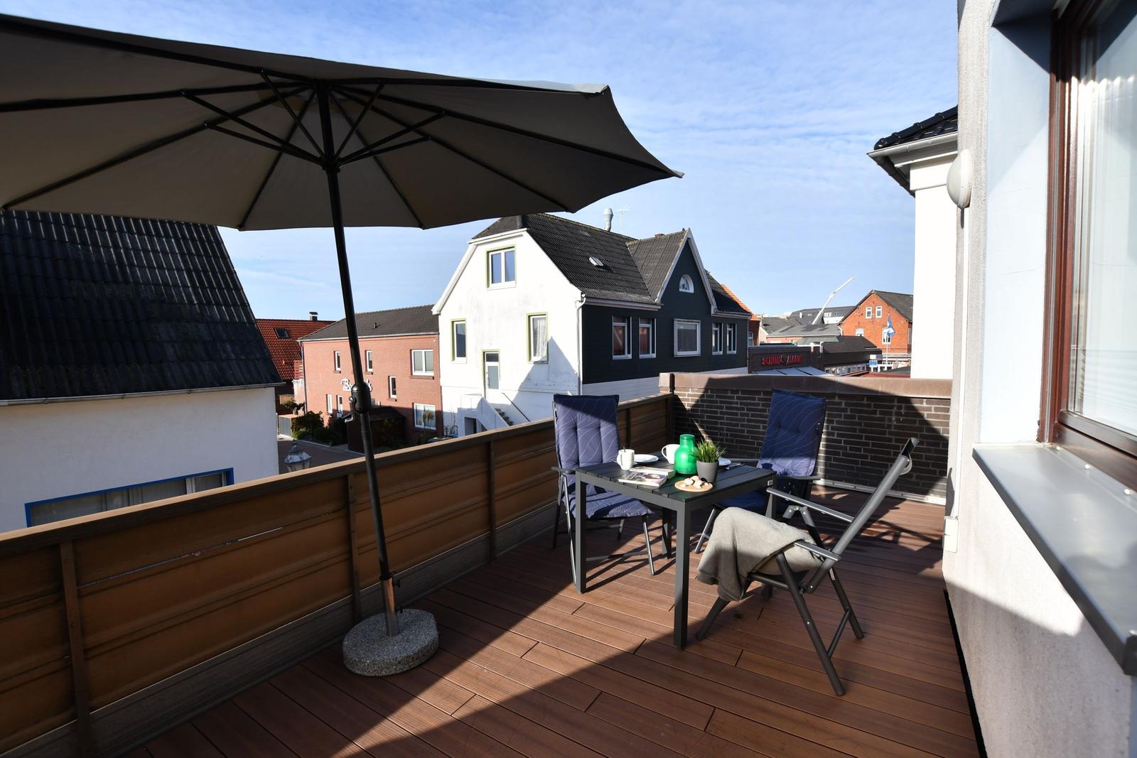 Terrasse mit Tisch, Stühlen und Sonnenschirm. Blick auf umliegende Häuser.