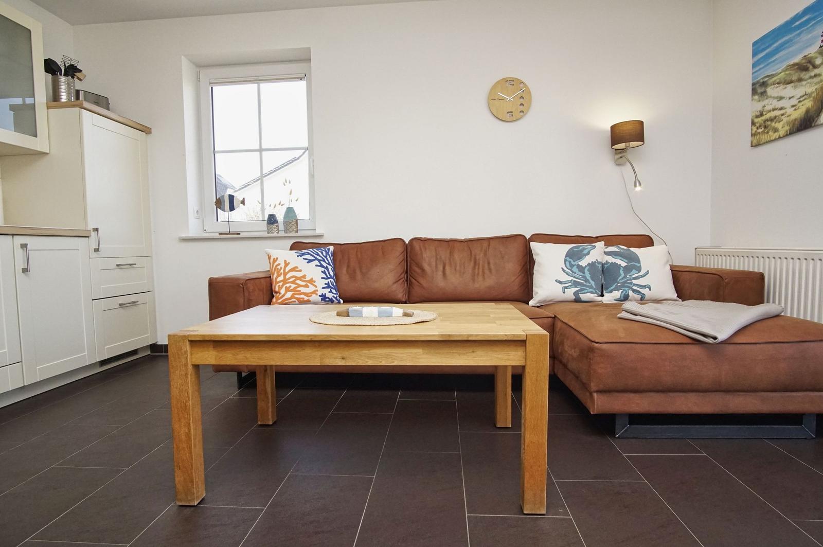 Ein Wohnzimmer mit braunem Sofa, Holztisch und Küchenzeile.