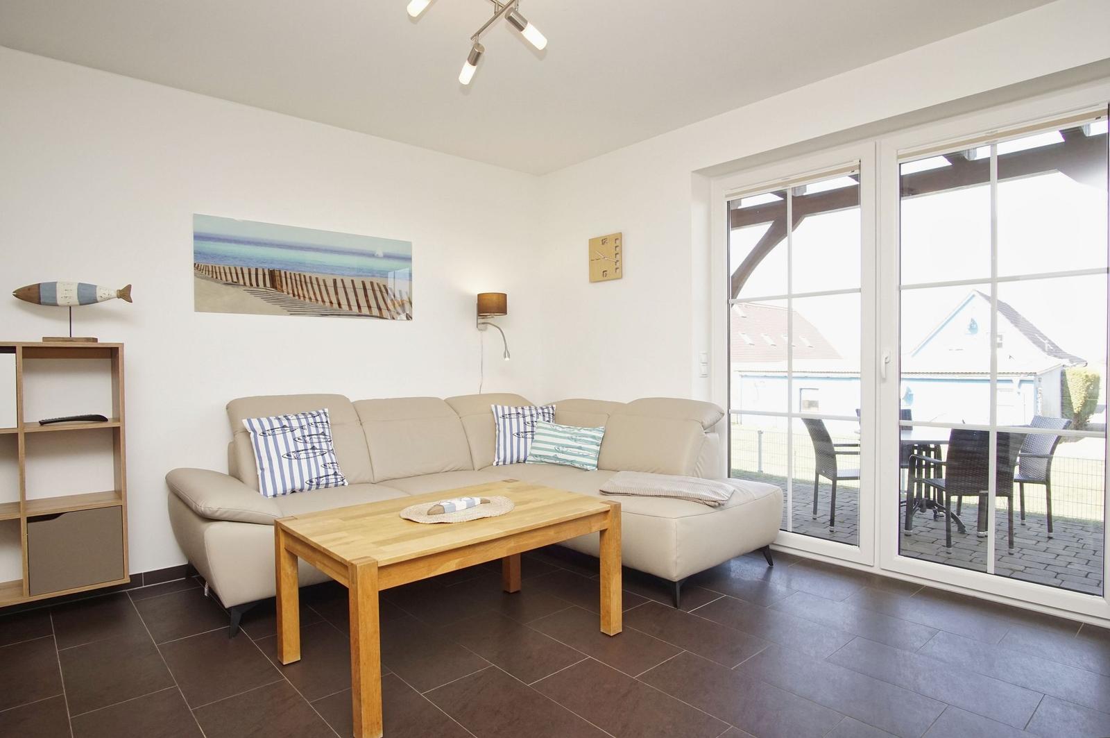 Wohnzimmer mit Sofa, Tisch und Terrasse. Wandbild und Bücherregal sichtbar.