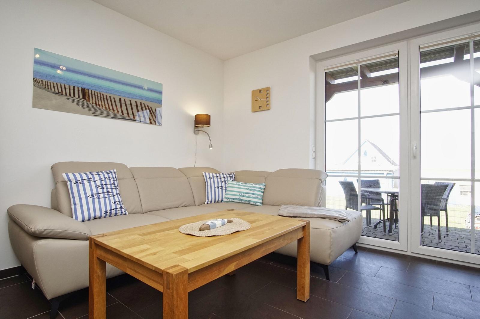 Wohnzimmer mit Sofa, Holztisch und Terrassentür. Wandbild und Wanduhr sind sichtbar.
