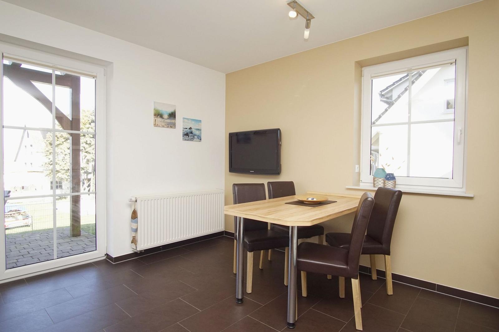 Esszimmer mit Tisch, vier Stühlen, Fernseher und Fenster zur Außenterrasse.