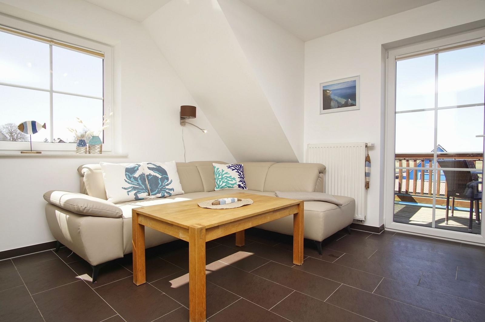 Wohnzimmer mit Sofa, Holztisch und Balkontür. Dachneigung und Fenster sichtbar.