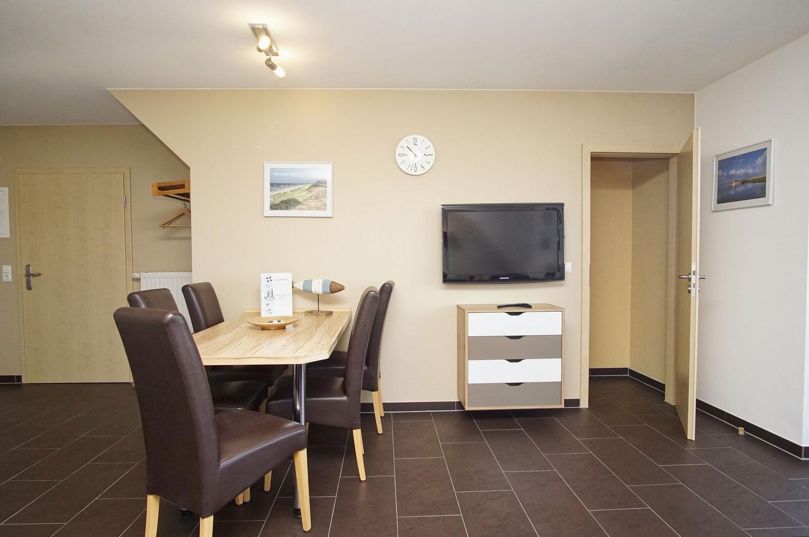Esszimmer mit Tisch, Stühlen, Fernseher und Schrank an der Wand.
