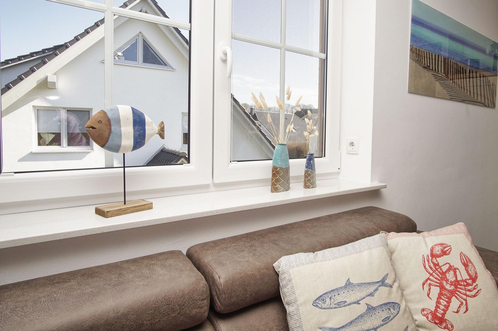 Sitzbank mit Kissen vor Fenster. Dekoration mit Fischfigur und Vasen.