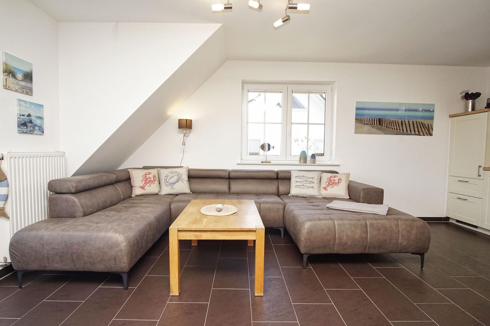 Wohnzimmer mit Ecksofa, Holztisch und Fenster. Wandbild und Heizkörper sichtbar.