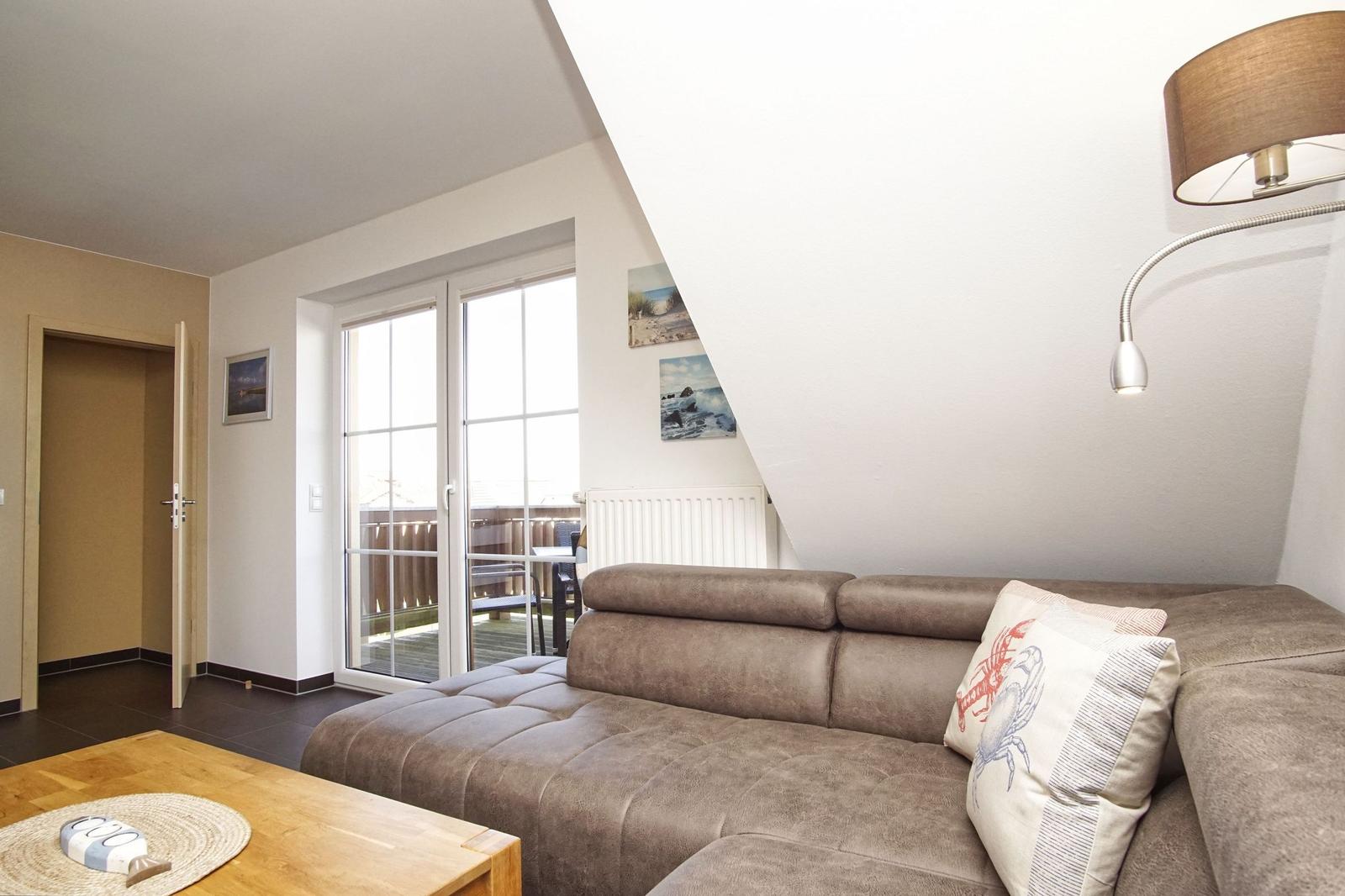 Wohnzimmer mit Sofa, Couchtisch und Balkontür. An der Wand hängen Bilder.