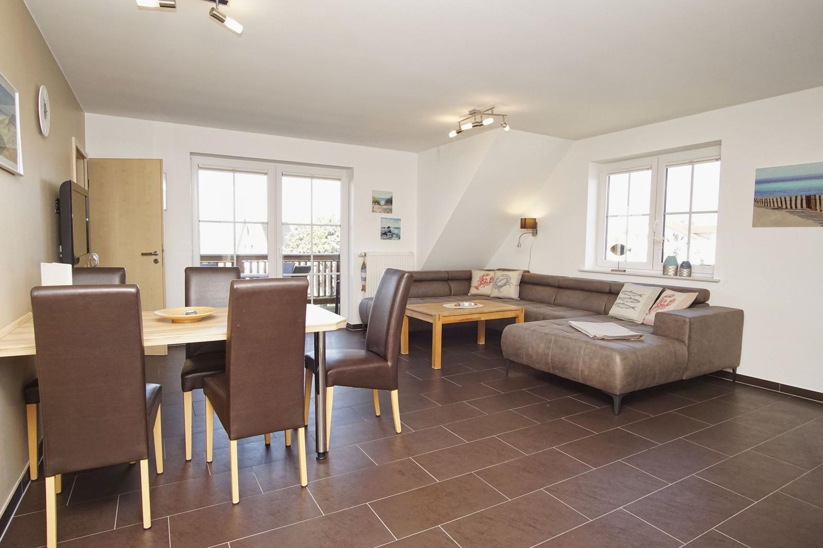 Wohn- und Essbereich mit Sofa, Tisch und Stühlen. Fenster und Balkontür.