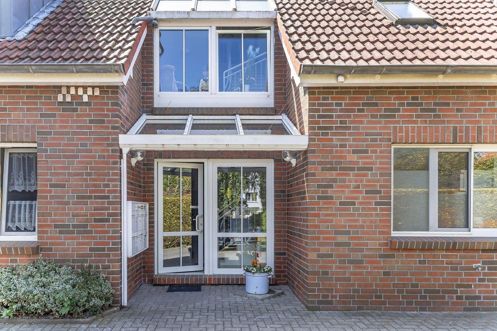 Eingangsbereich mit Glas-Tür und Terrasse. Haus mit Ziegelfassade und Dachgauben.
