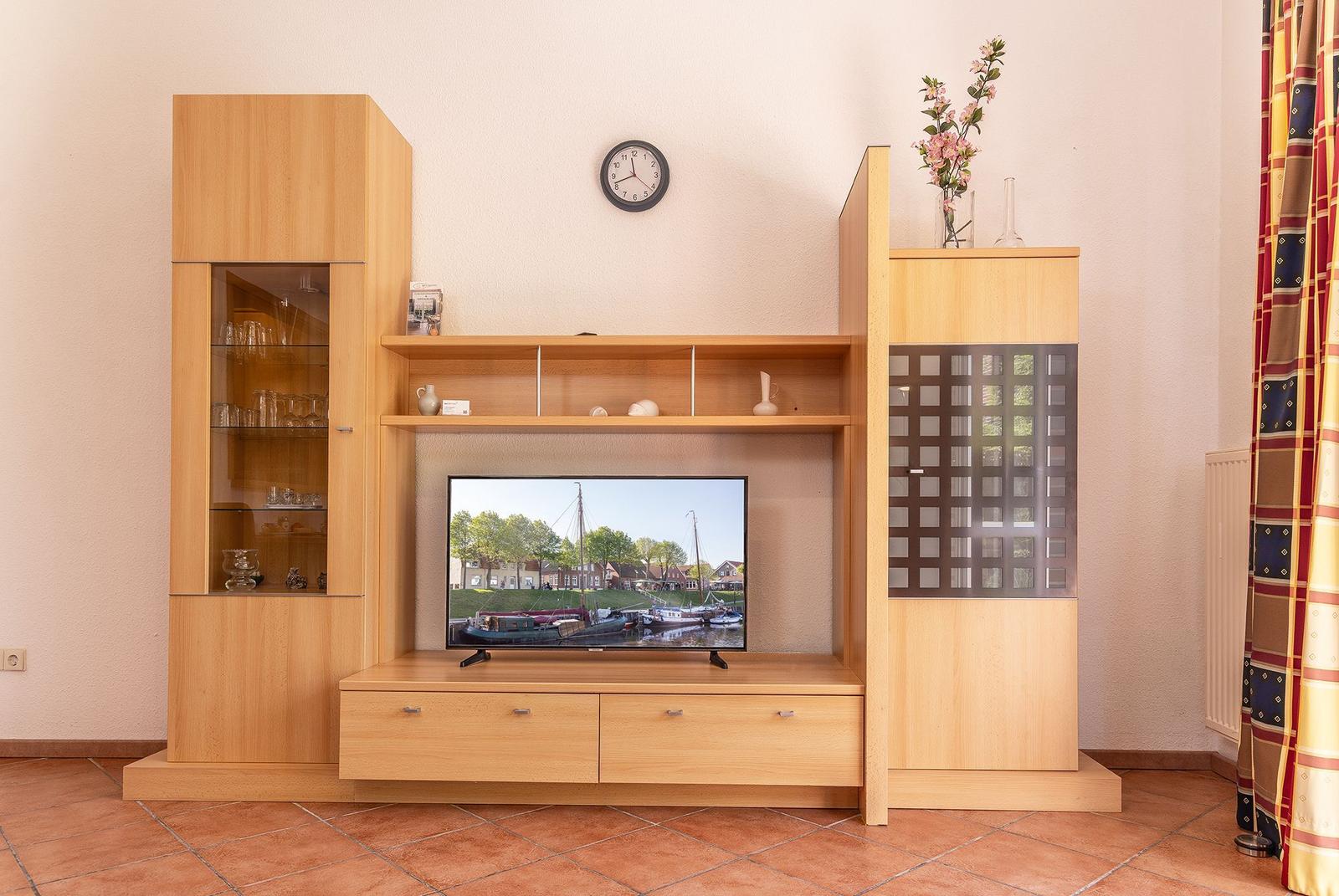 TV-Möbel mit Glasfront, Schubladen und Dekorationsgegenständen an der Wand.