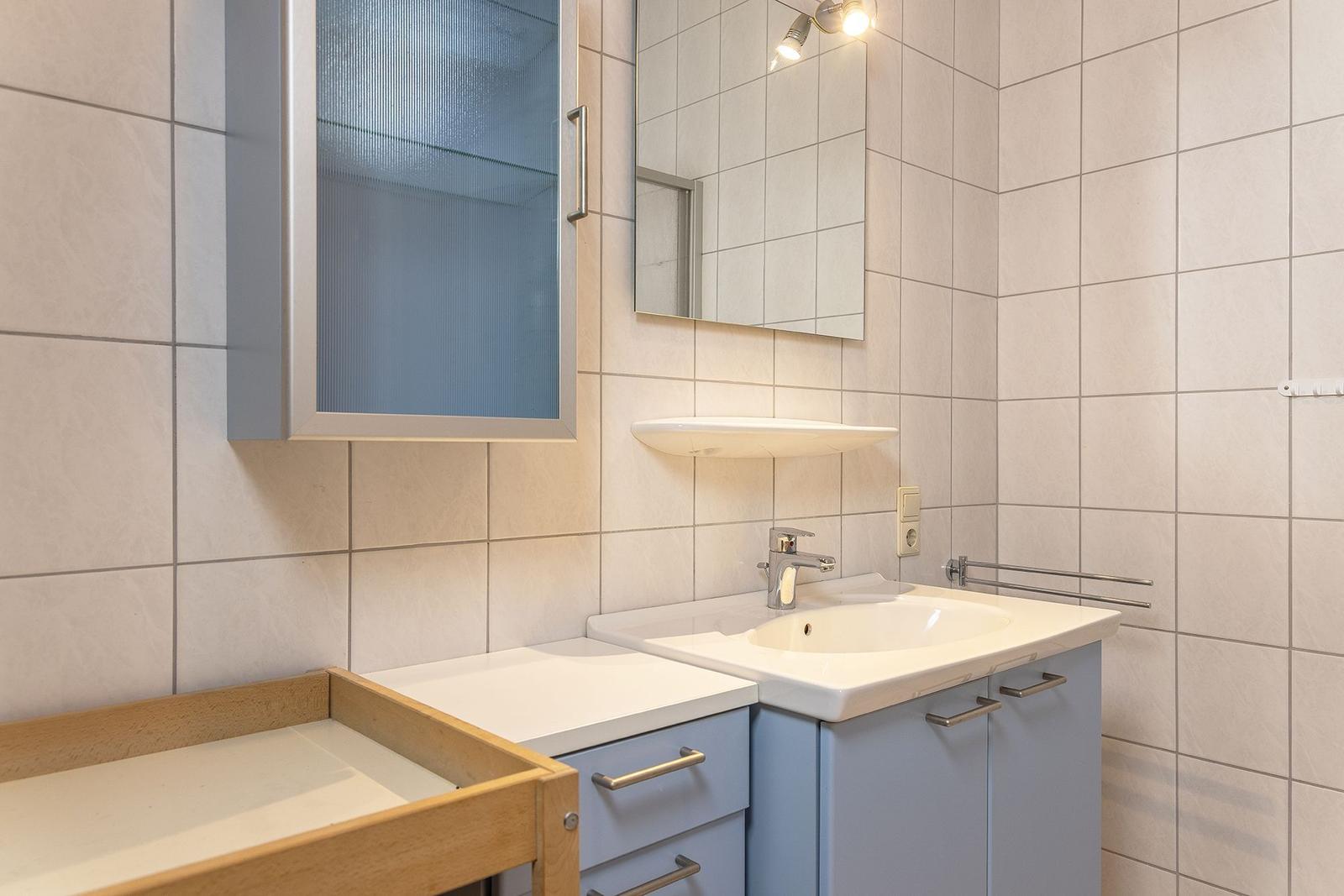 Badezimmer mit Waschbecken, Spiegel und Aufbewahrungskasten.