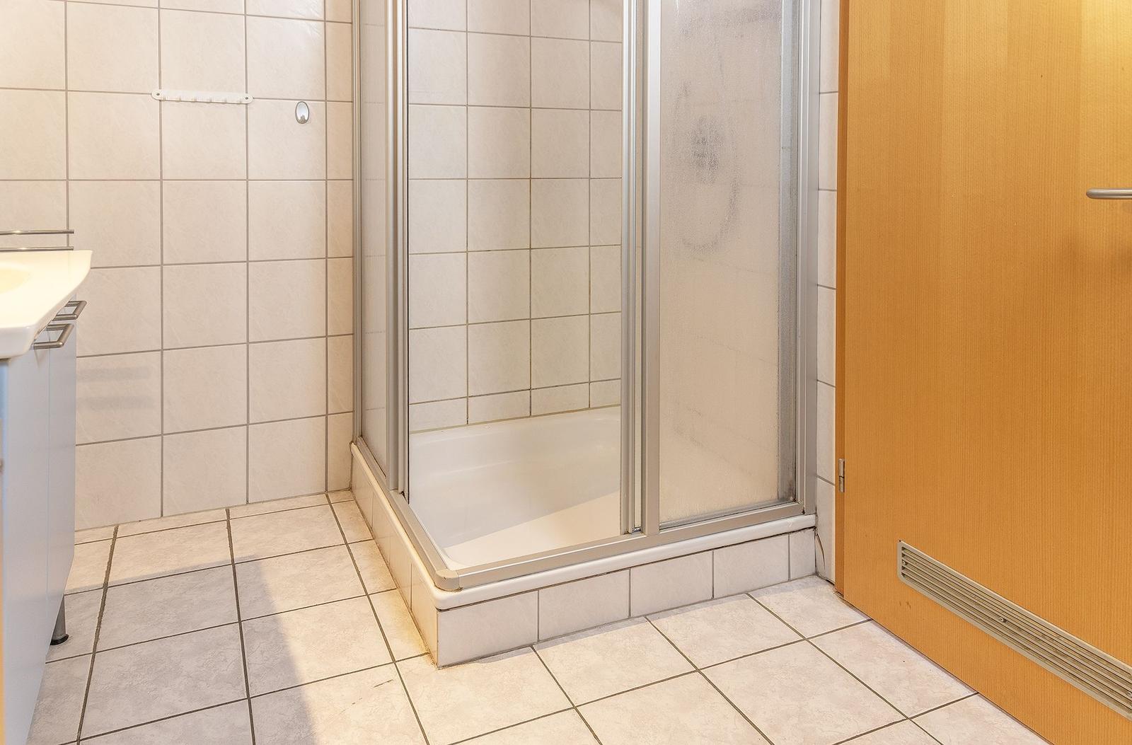 Badezimmer mit Dusche, Waschbecken und Holztür