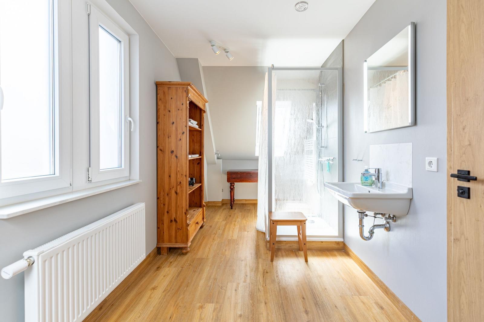Bathroom with shower, sink, and wooden cabinet against the wall.