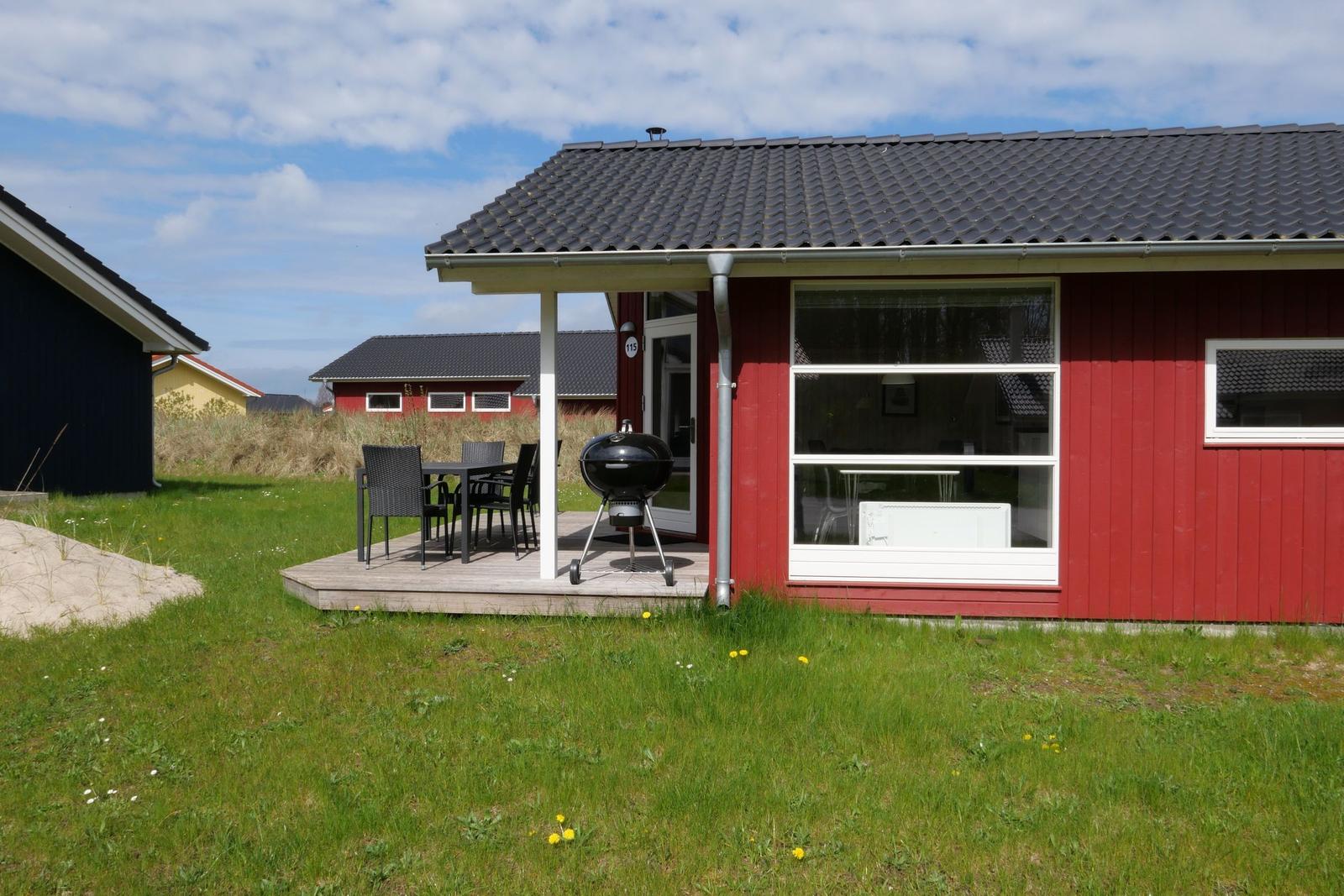 Rotes Ferienhaus mit Terrasse, Grill und Sitzgelegenheit im Garten.