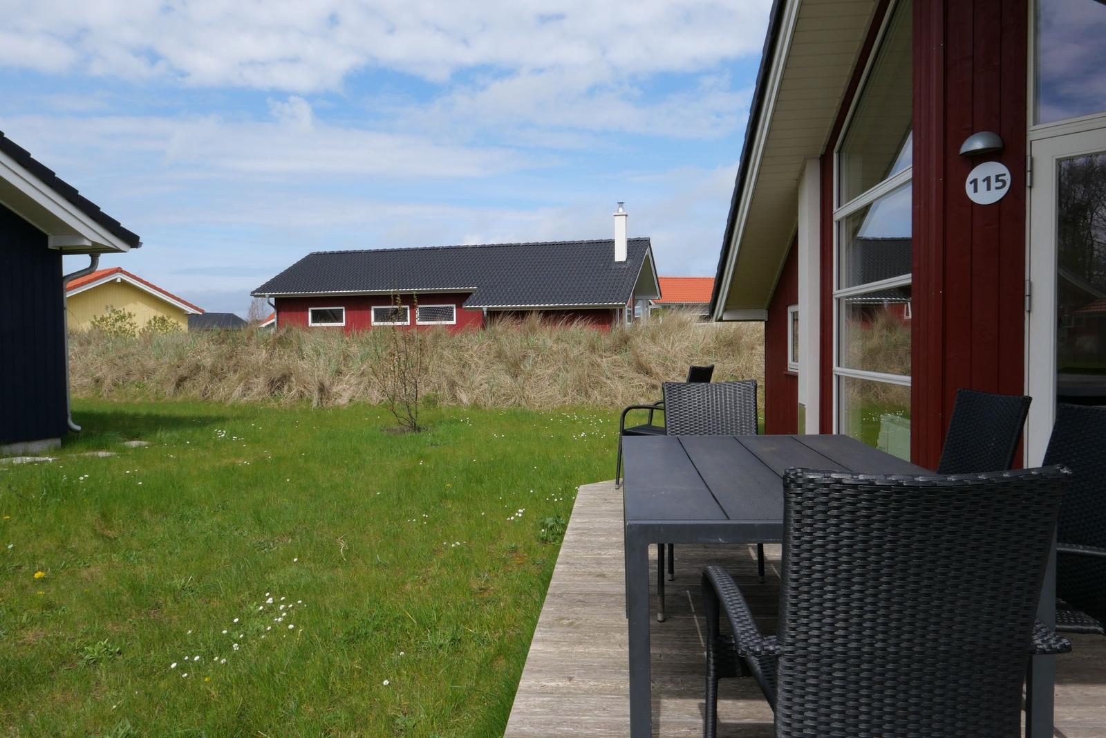 Terrasse mit Tisch und Stühlen vor einem roten Haus mit Hausnummer 115.