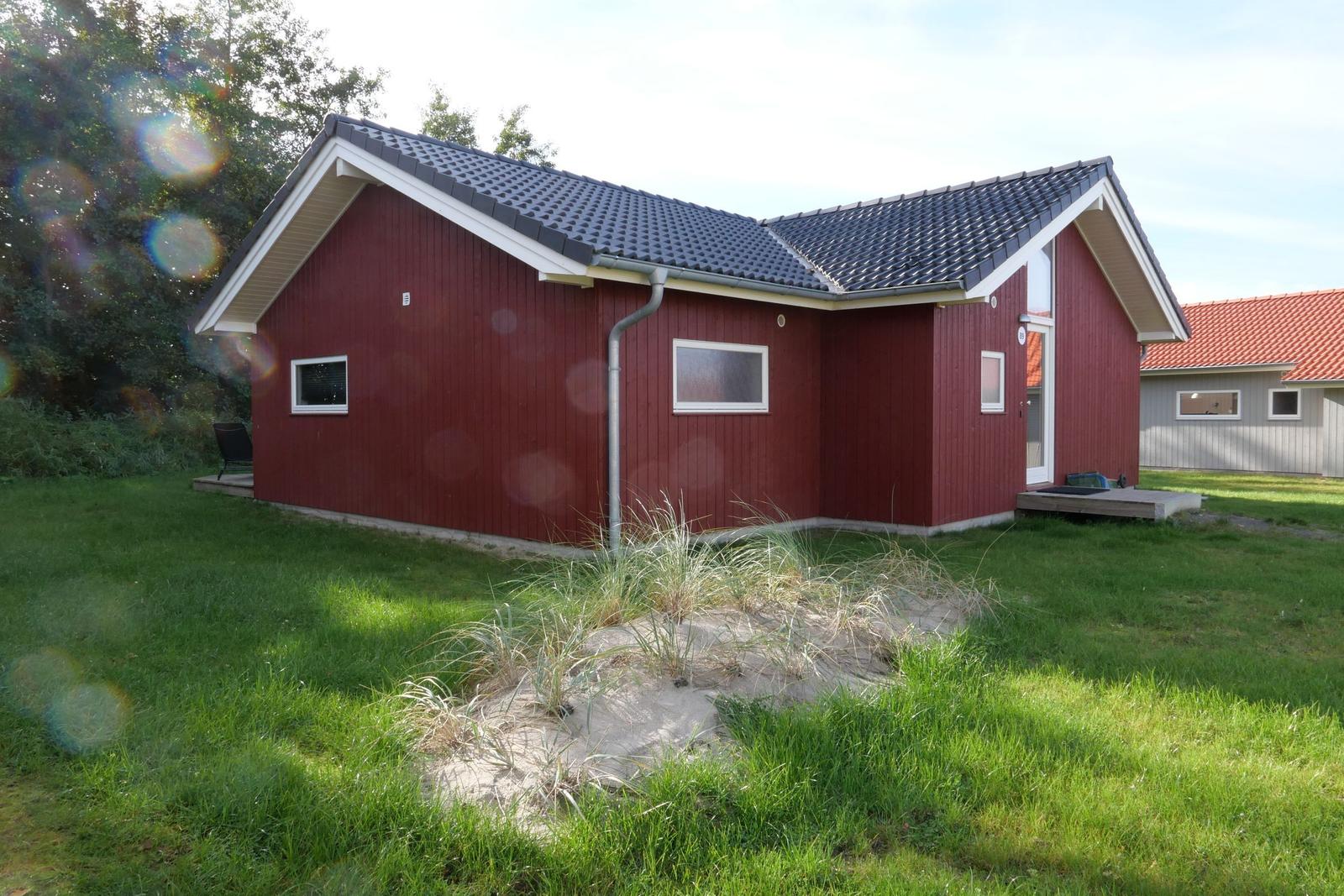 Rotes Holzhaus mit dunklem Dach und grünem Garten. Eingang mit kleinen Plattform.