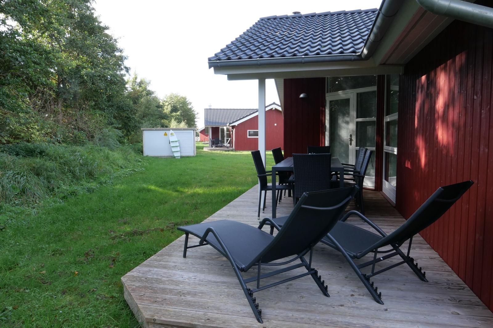 Terrasse mit Liegestühlen und Tisch vor rotem Holzhaus mit Garten.