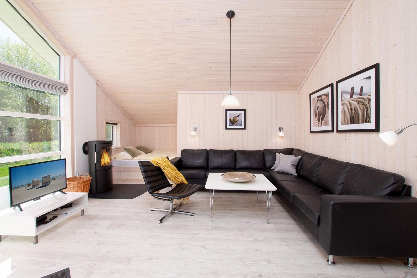 Wohnraum mit Sofa, Fernseher und Kamin. Holzwände und große Fenster.