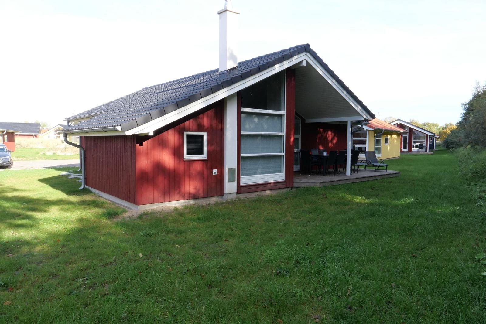 Rotes Ferienhaus mit Terrasse und Garten. Holzverkleidung und dunkler Dachziegel.