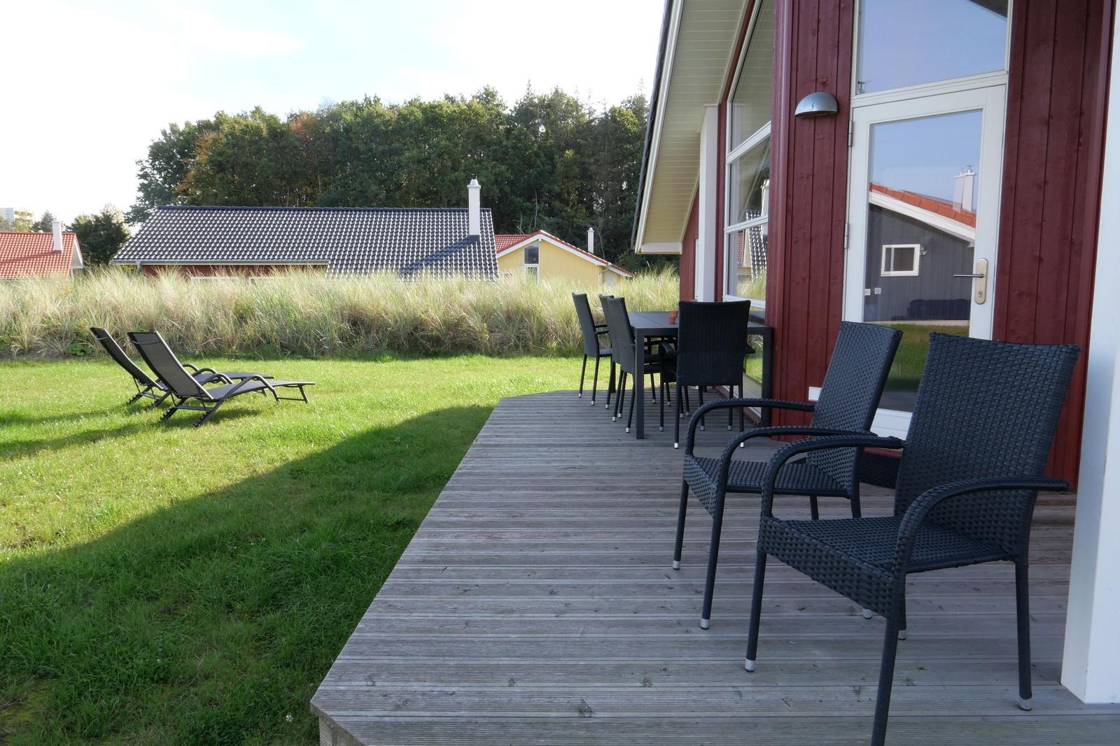 Deck with table and chairs, lounge chairs on lawn, view of grass and houses.
