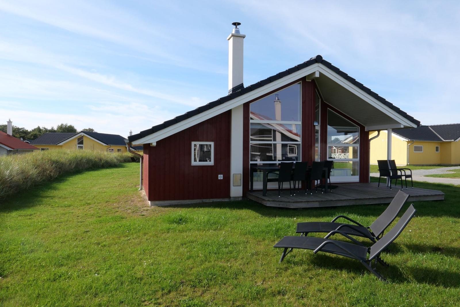 Red cabin with terrace and garden. Black lounge chairs and table outside.