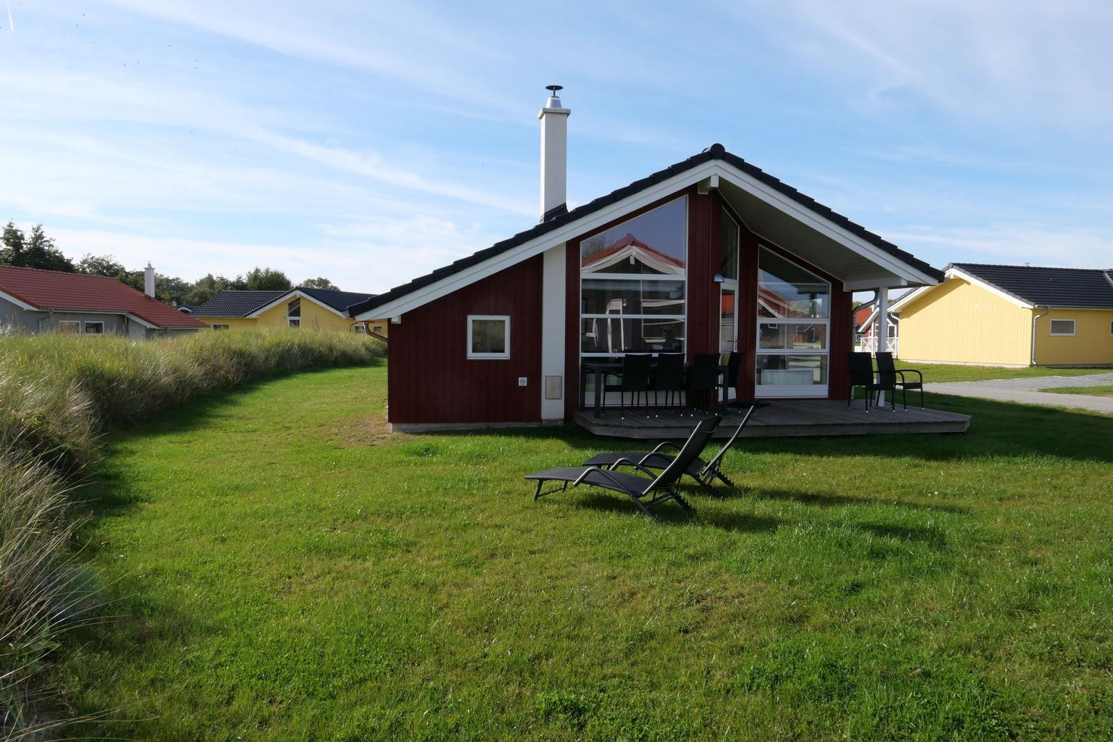 Red wooden house with terrace and sun loungers on green lawn.