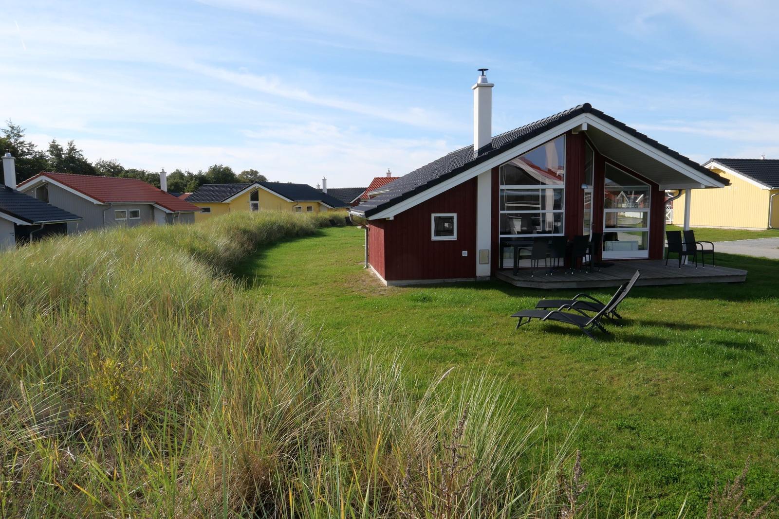 Red vacation house with terrace and lounge chairs on green lawn.