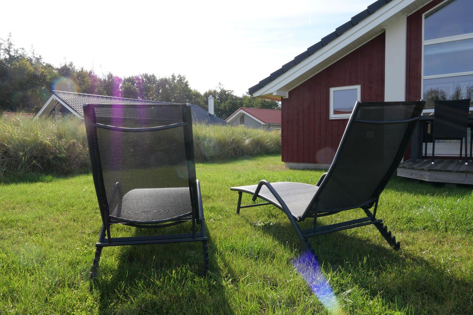 Two black lounge chairs on green grass in front of a red house.