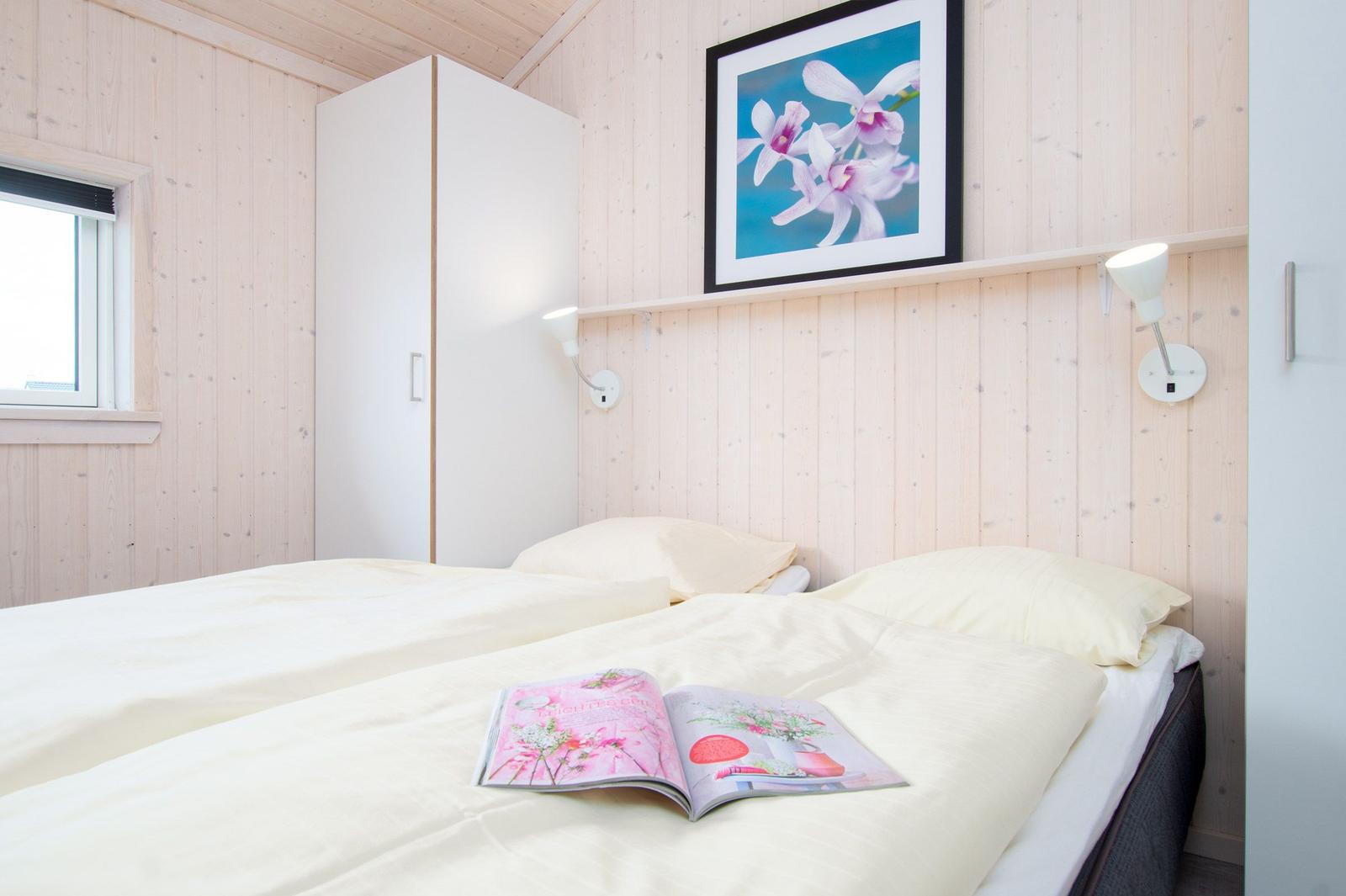 Bedroom with bed, wardrobe, and wall art. A magazine lies on the bed.