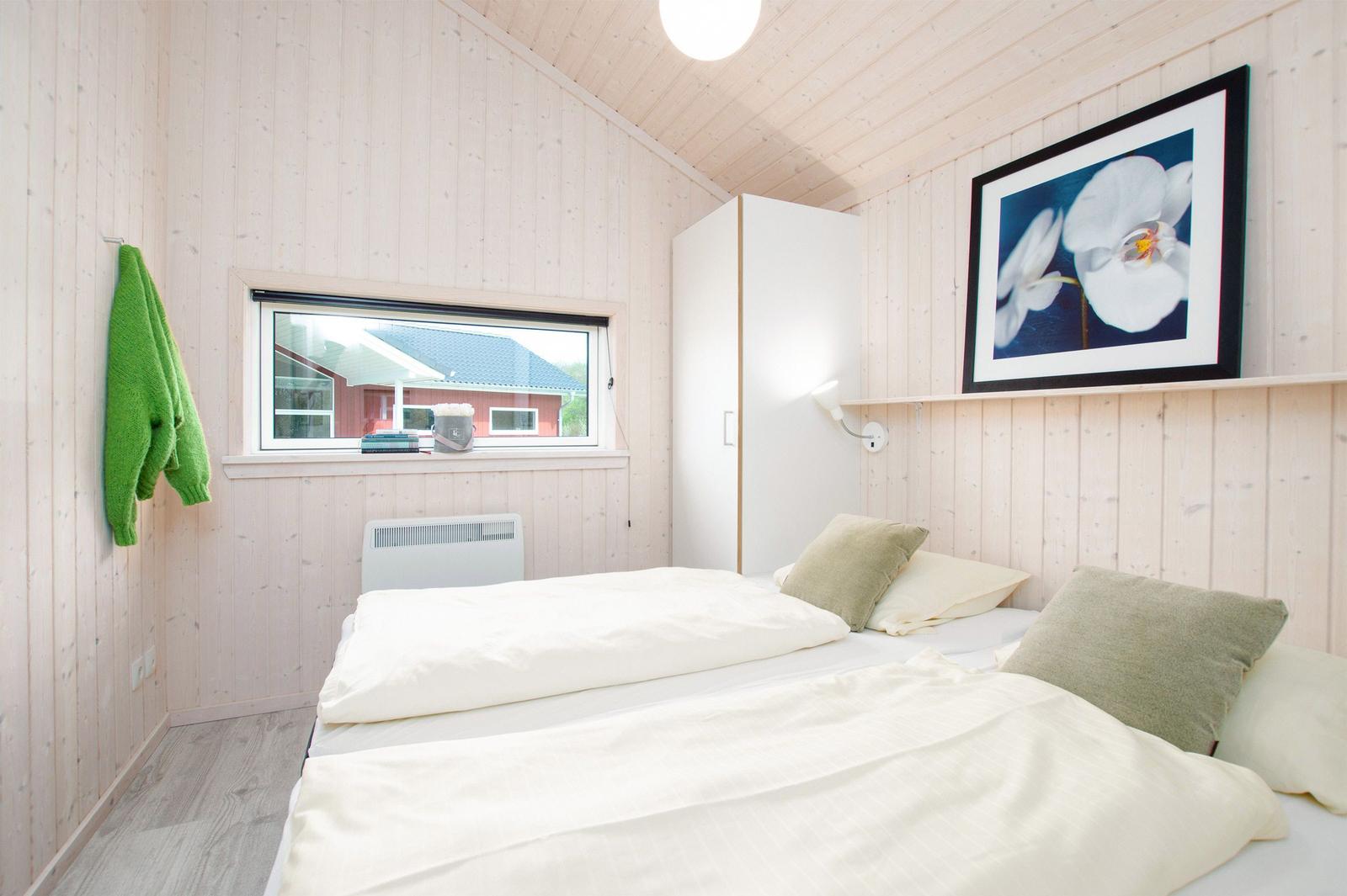 Schlafzimmer mit Bett, Fenster und Wandbild. Holzwände und weißer Schrank.