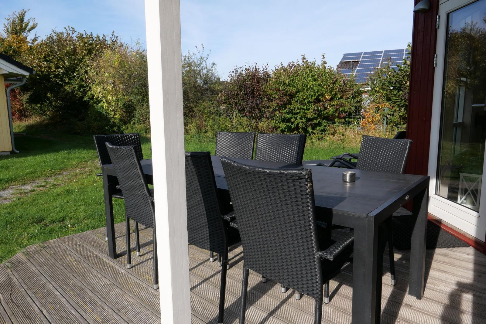 Terrasse mit Esstisch und sechs Stühlen, Blick auf Grünflächen und Solaranlage.