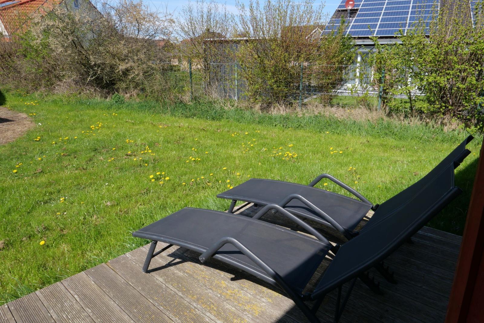 Zwei Liegestühle auf einer Holterrasse mit Blick auf einen grünen Rasen mit gelben Blumen.