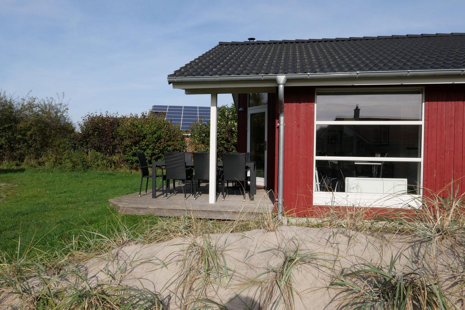 Rotes Haus mit Terrasse, Tisch und Stühlen. Im Hintergrund Solaranlage und Grünfläche.