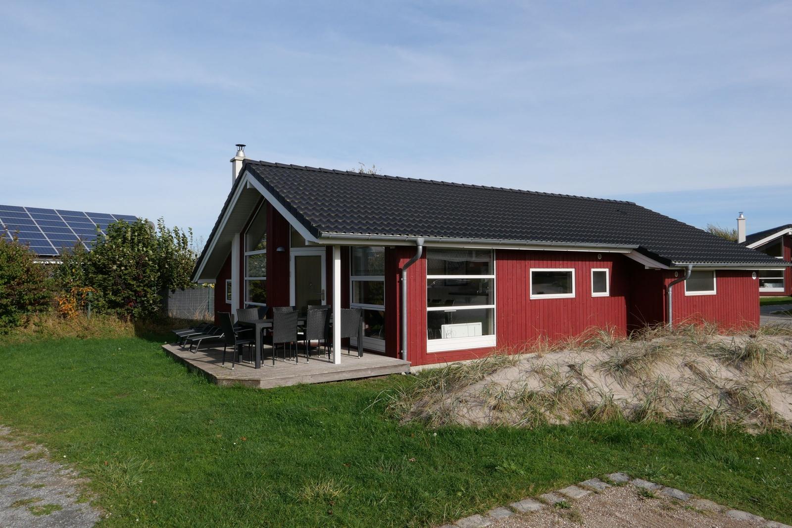 Rotes Ferienhaus mit Terrasse und Garten. Solaranlage im Hintergrund.