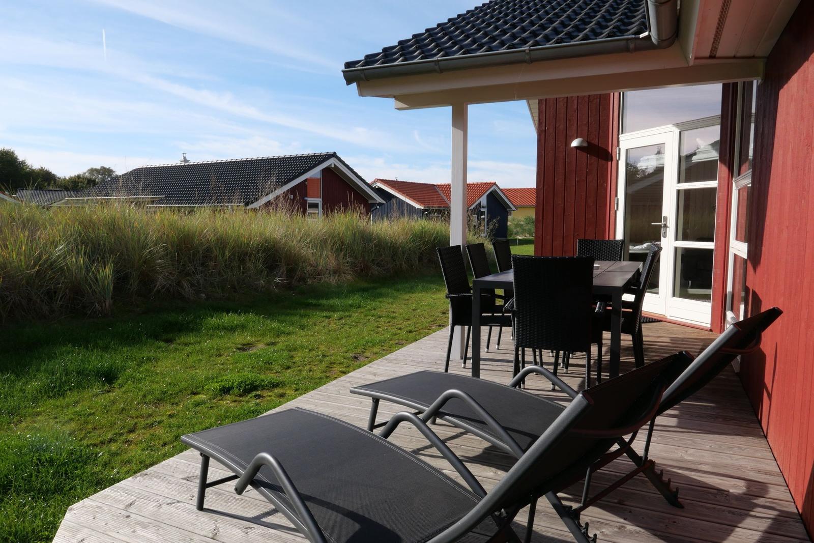 Terrasse mit Liegestühlen und Tisch. Hintergrund: Gras und Häuser.