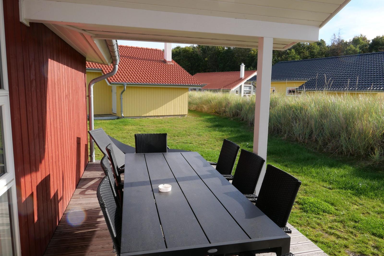 Terrasse mit Tisch und Stühlen, Blick auf grünen Rasen und gelbe Häuser.