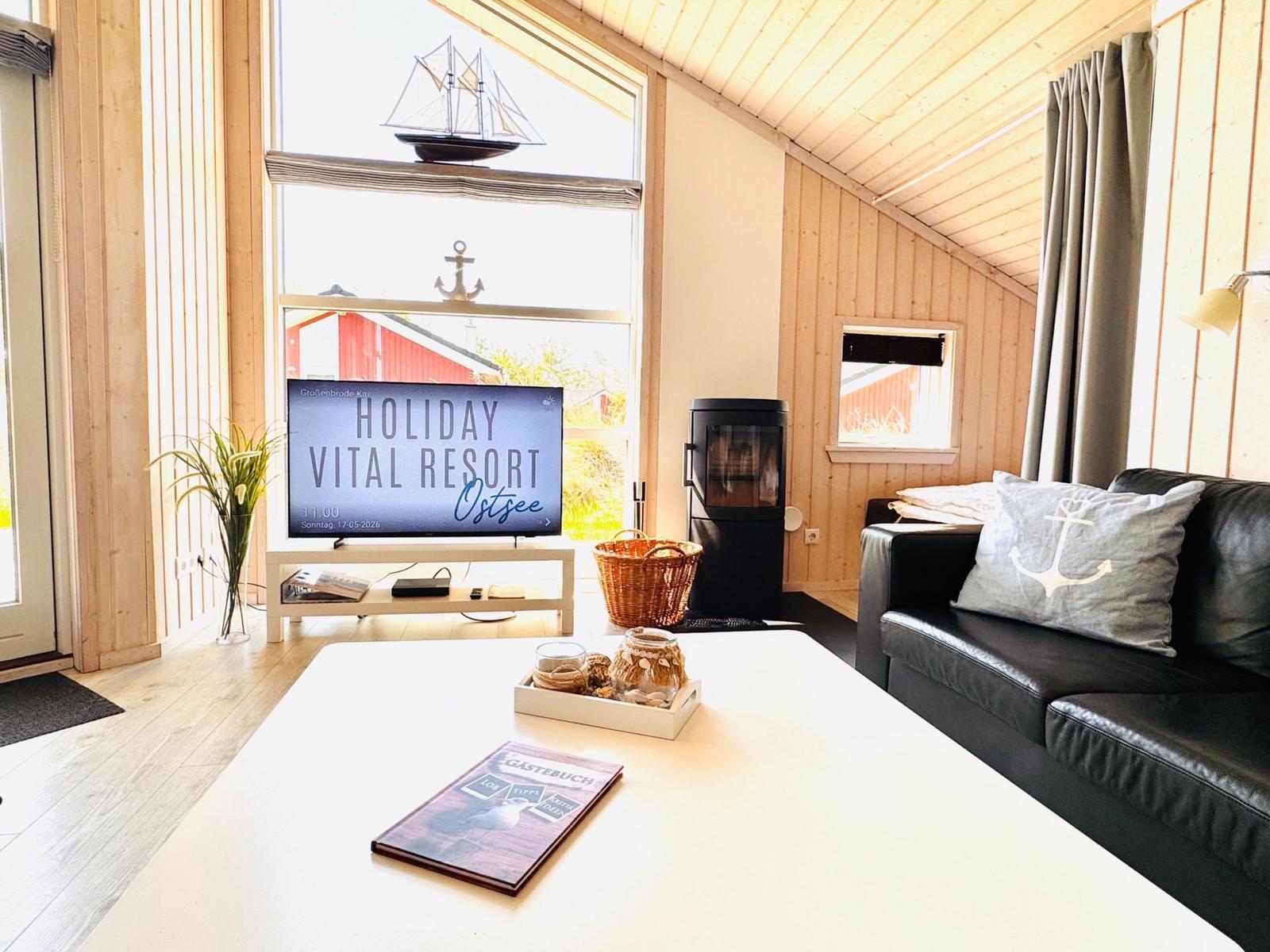 Wohnzimmer mit Sofa, Fernseher und Holzwand. Fenster mit Segelboot-Dekoration.