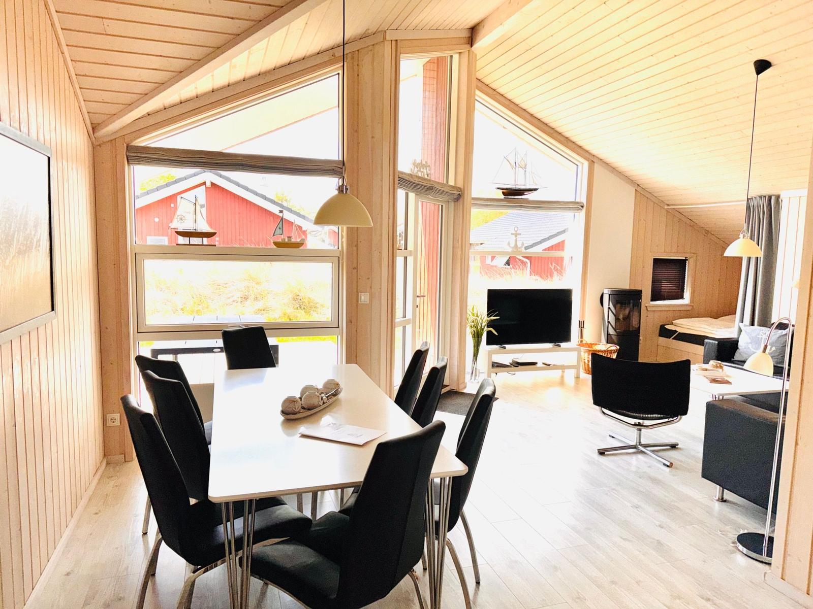 Essbereich mit Tisch und Stühlen. Wohnbereich mit Fernseher und Sofa. Holzwände und große Fenster.