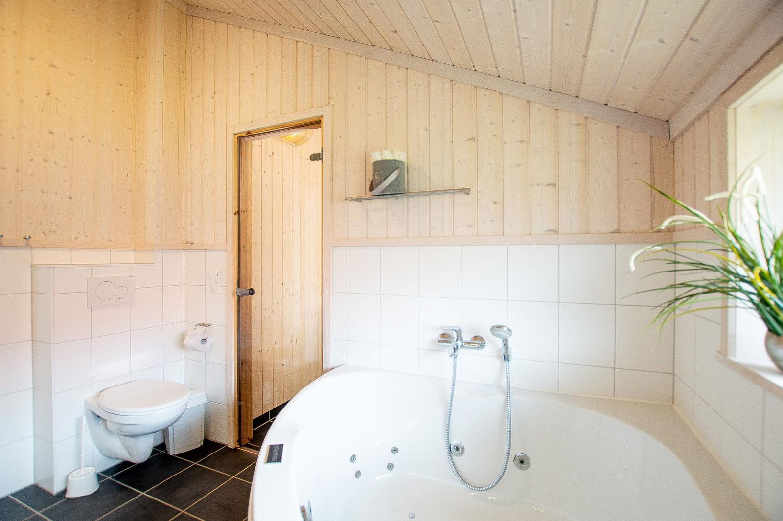 Bad mit Whirlpool, Toilette und Pflanze. Holzwände und Fliesen.