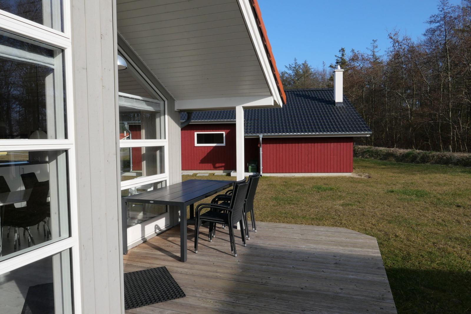 Terrasse mit Tisch und Stühlen vor einem Haus mit rotem Anbau.