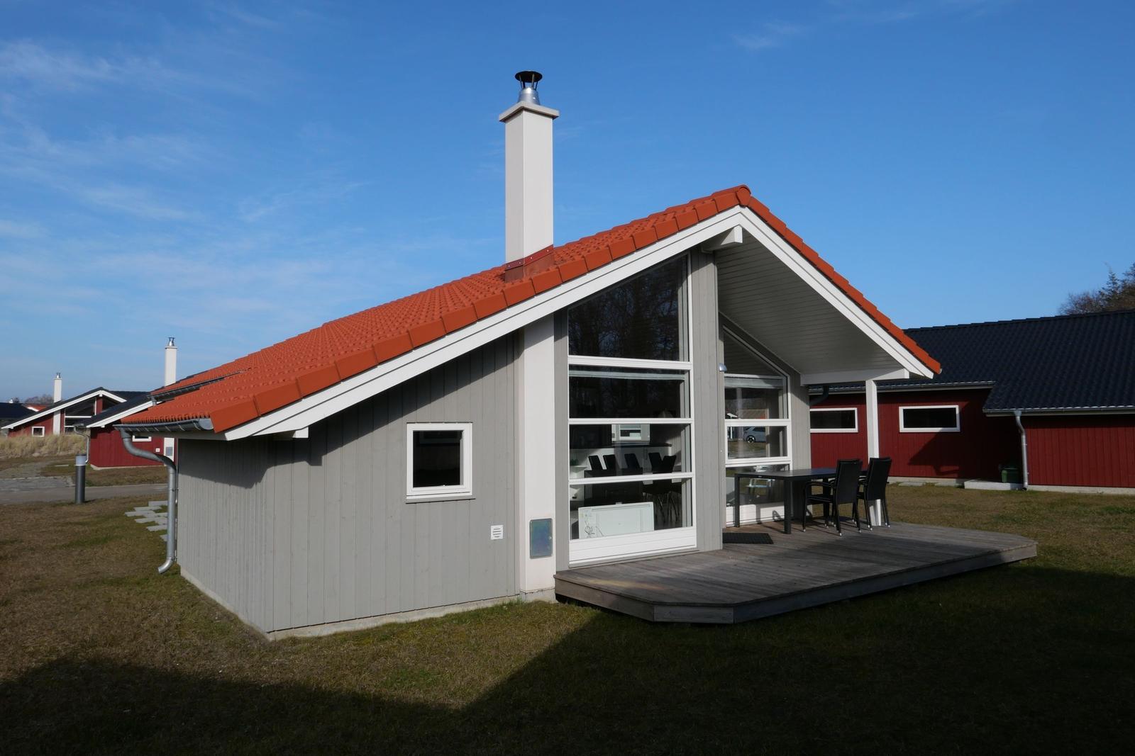 Moderne Holzhütte mit rotem Dach und Terrasse mit Tisch und Stühlen.