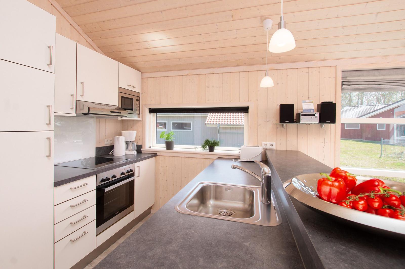 Küche mit Holzwand, Arbeitsplatte und Fenster. Auf der Arbeitsplatte steht eine Schale mit Tomaten.