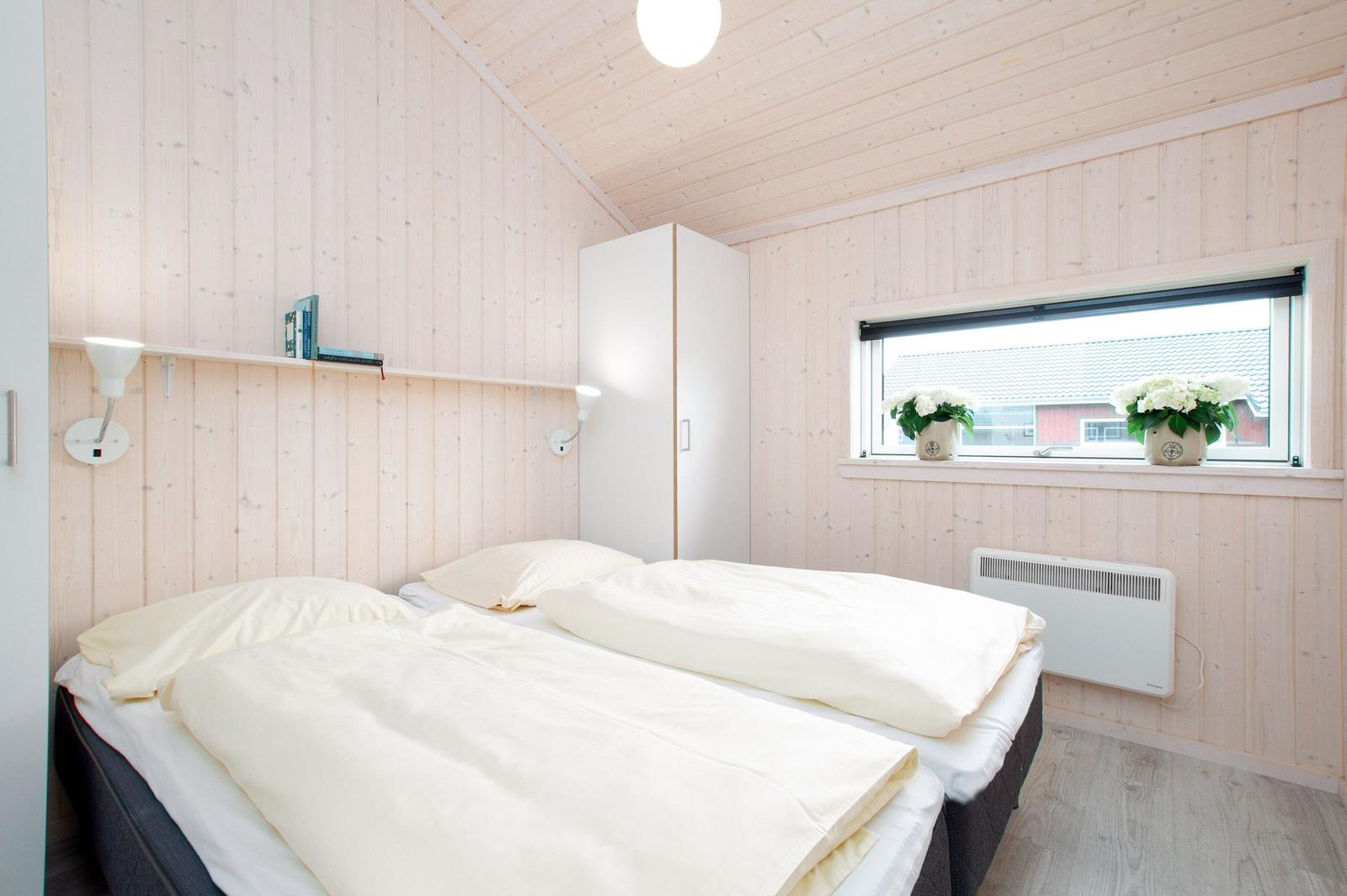 Schlafzimmer mit Doppelbett, Holzwand und Fenster mit Blumen.