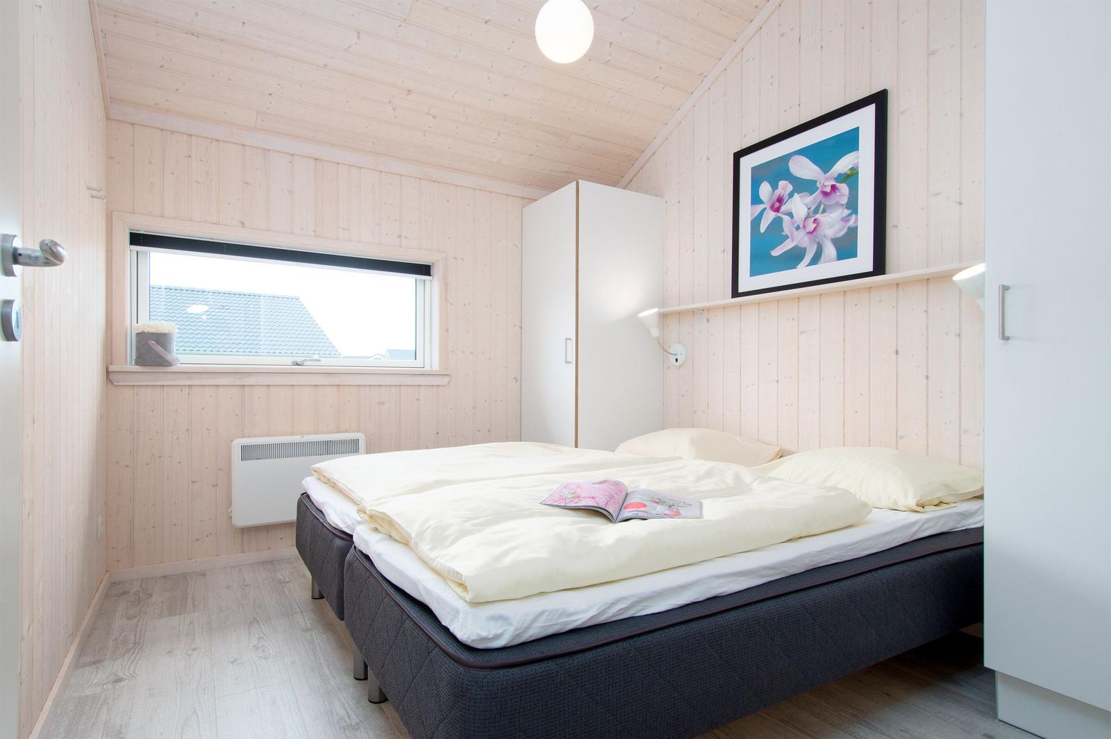 Schlafzimmer mit Bett, Fenster, Schrank und Wandbild.