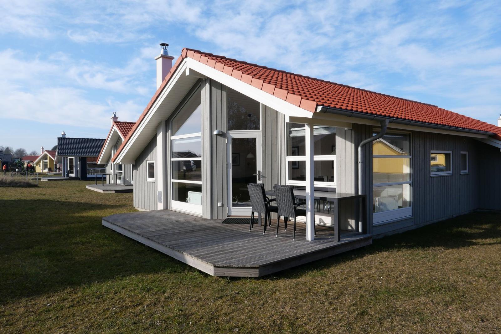 Moderne Ferienhaus mit Holzterrasse und großem Fensterbereich unter rotem Dach.