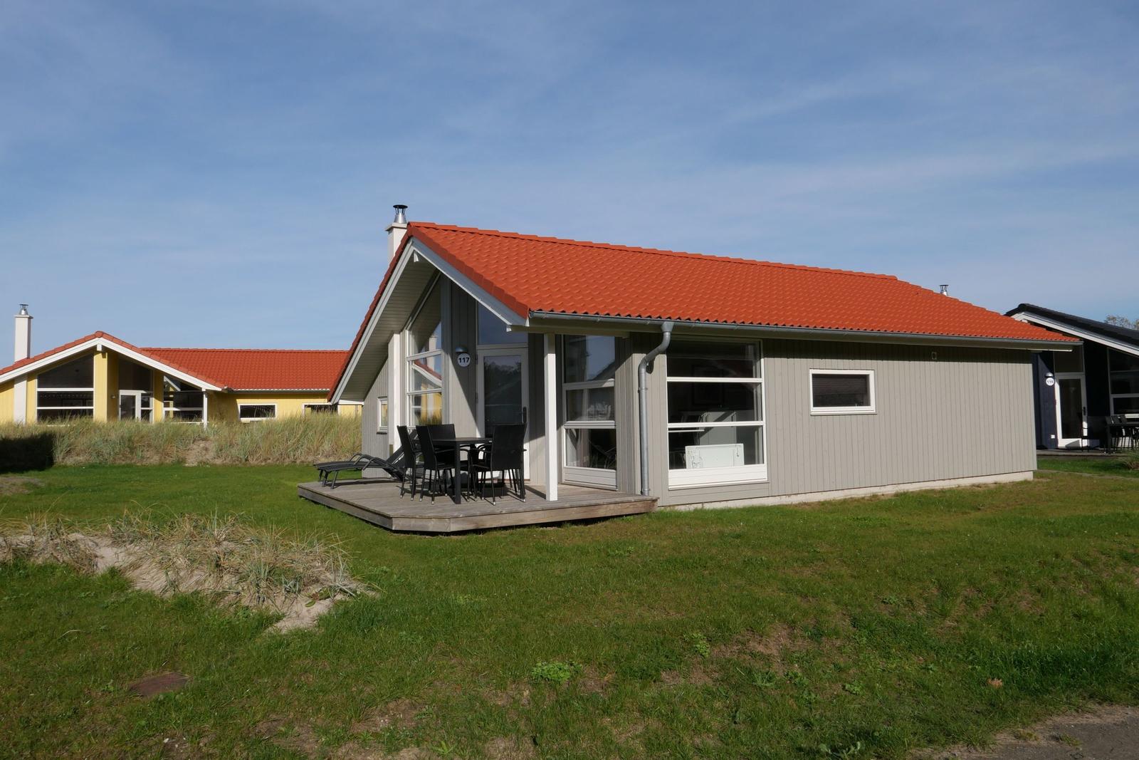 Moderne Ferienhaus mit Terrasse, Garten und rotem Dach.