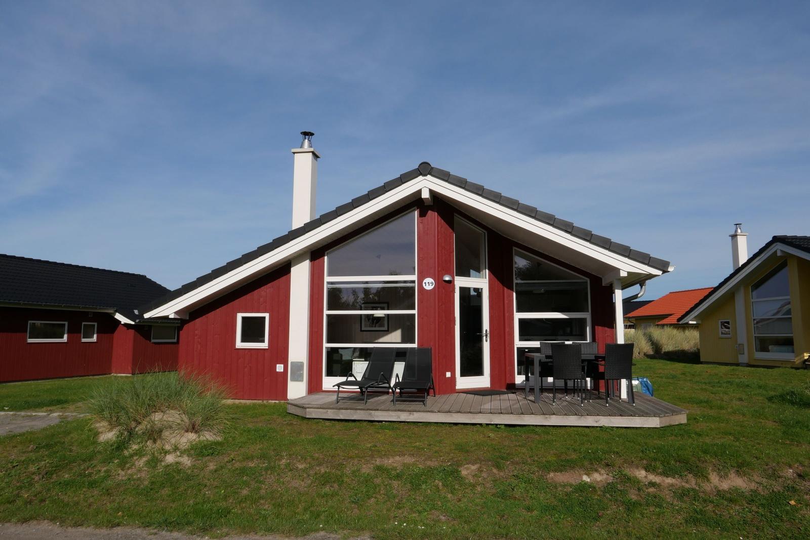 Rotes Ferienhaus mit Terrasse, Garten und großem Fenster. Hausnummer 119.