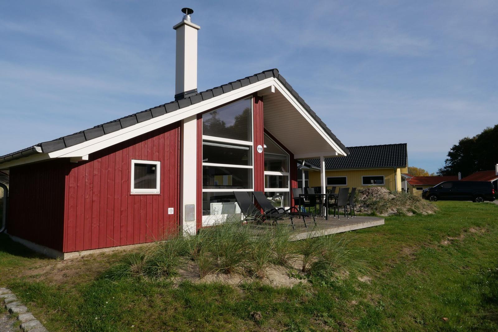 Rotes Holzhaus mit Terrasse und Garten. Schwarzer Dachfirst und weißer Schornstein.